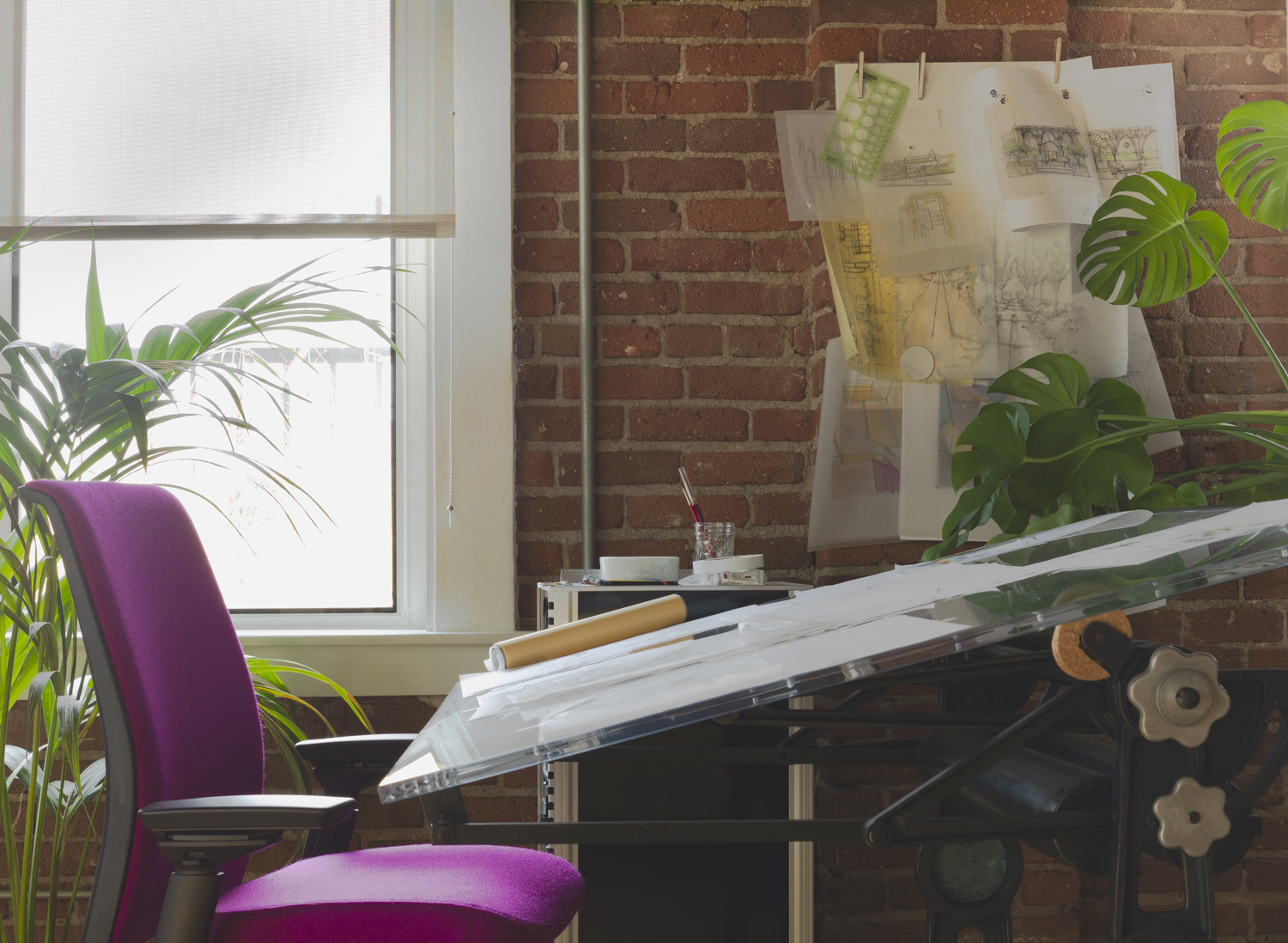 An interior view of the WVH Design studio; a purple architect's chair at an antique drafting table covered in drawings and surrounded by tropical plants.